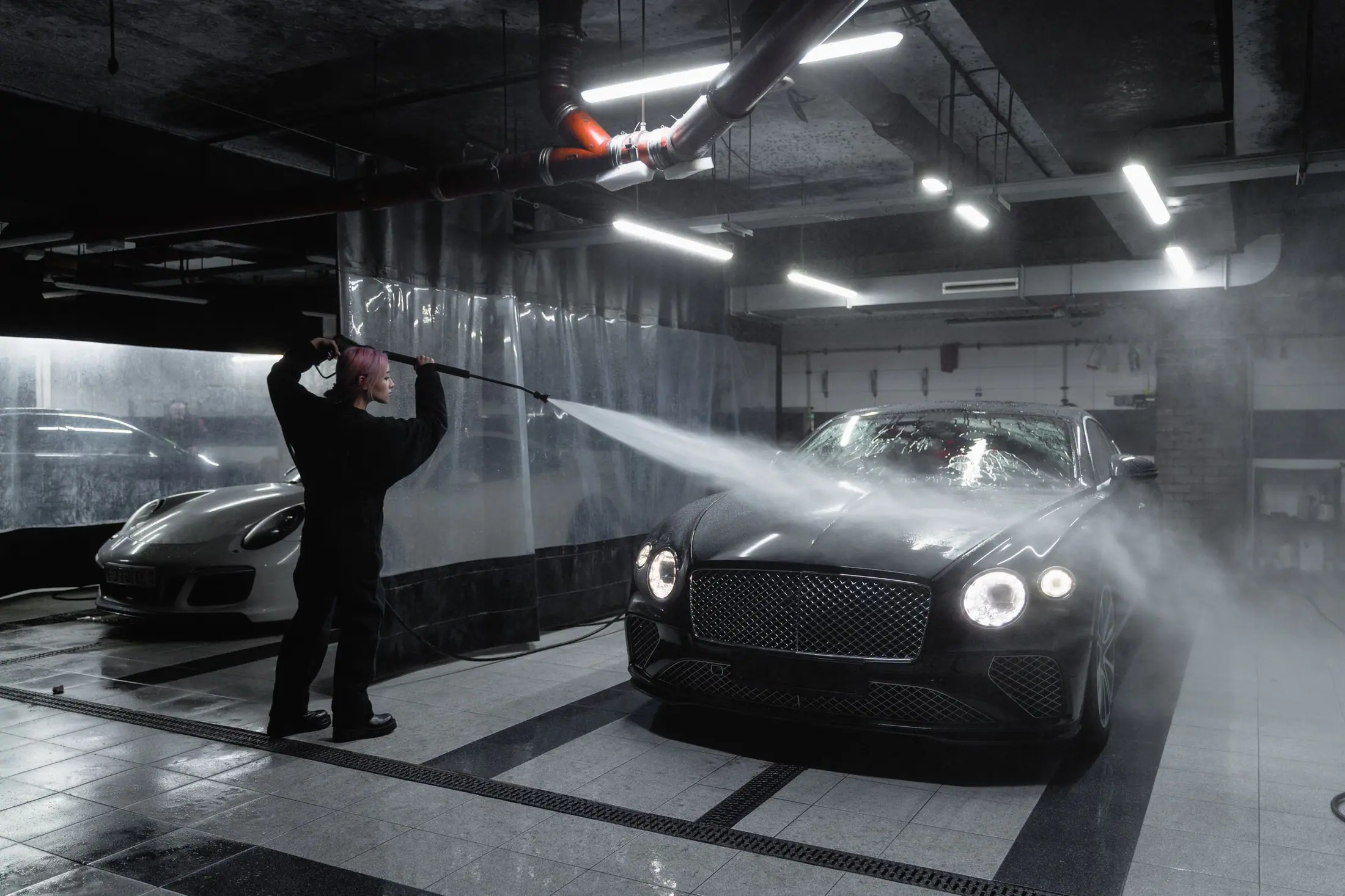 A black luxury car being pressure-washed in a basement parking bay